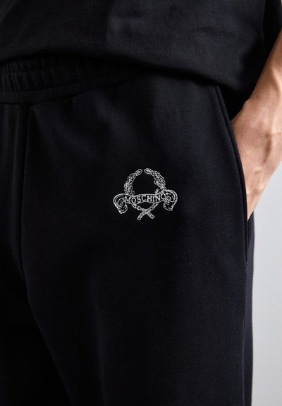 Melni sporta bikses ar izšūtu logotipu, kurā ir savītas virves un "Moschino" teksts. Mīksta auduma, ar elastīgu jostu un sānu kabatu.