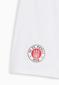Biela tkanina so zaobleným logom na červenom pozadí, dizajnom hradu a textom "FC ST. PAULI 1910" v hnedej farbe.