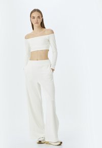 Witte off-shoulder crop top gecombineerd met witte wijde broek met elastische tailleband. Zacht, glad materiaal; geen zichtbare patronen.