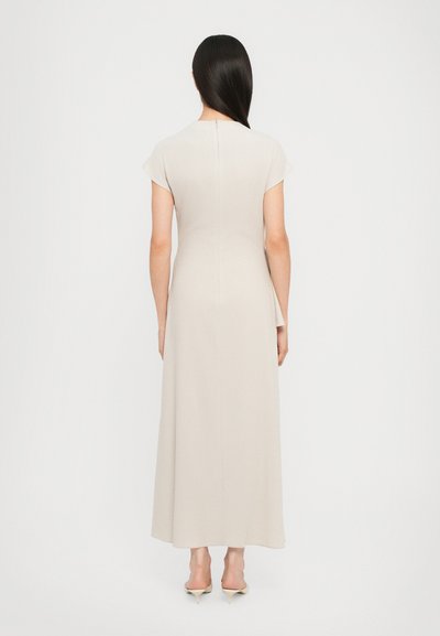 Long, beige dress with cap sleeves and a fitted silhouette. Smooth texture with a center back zipper. Shoes are open-toed heels.