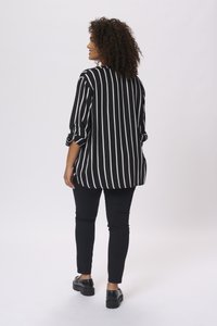 Black and white striped oversized blouse with rolled sleeves, paired with black skinny pants and black platform shoes. White background.