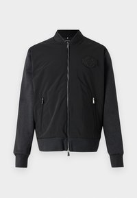 Black bomber jacket with a zip front, ribbed cuffs, and a textured fabric design. Featuring a logo patch on the left chest.