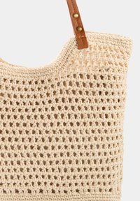 Torebka typu tote w odcieniu beżowym, z teksturowanym wzorem z otwartym splotem oraz brązowym paskiem na ramię z ekoskóry z mosiężnymi akcentami.