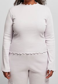 Ljuslila ribbad långärmad topp med en volangkantad halsringning och nederkant, med figursydda ärmar och en mjuk textur.