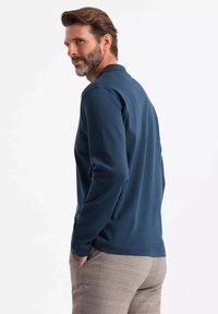 Marineblaues Langarm-Polohemd mit weichem Material, ausgestattet mit einem Kragen und lockerem Schnitt, kombiniert mit hellen karierten Hosen.