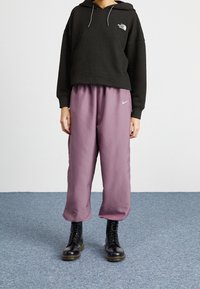 Svart hoodie med våffeltextur, grå snören, matchad med lösa lila satinklänningar med en liten Nike-logotyp och svarta snörstövlar.