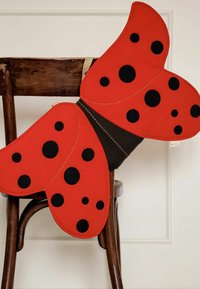 Red butterfly-shaped cushion with black polka dots, a black center, and stitched accents, placed on a wooden chair against a neutral background.