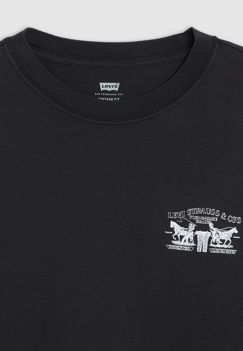 Camiseta de algodón negra con cuello redondo acanalado, que presenta una impresión gráfica vintage en blanco de caballos y una marca en el lado izquierdo del pecho.