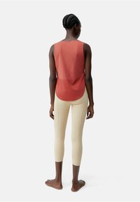 Rode mouwloze top met een afgeronde achterkant, gecombineerd met lichtbeige legging. Maak een gladde textuur en een aansluitend ontwerp, met zijzakken.