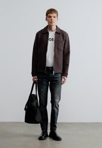 Sötétbarna cipzáras dzseki zsebbel, fehér póló fekete nyomattal, szakadt kék farmer, fekete csizma és fekete táska.