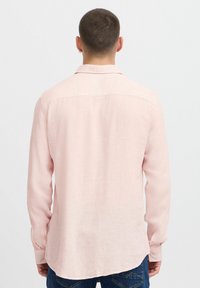 Chemise rose à manches longues en tissu texturé, col à boutons et ourlet arrondi. Comprend des poignets et un motif à rayures subtil.