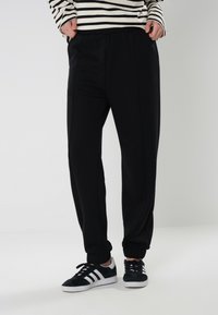 Sorte joggebukser med elastiske mansjetter og sidesømmer, laget av mykt stoff. Kombinert med svart-hvite joggesko og en stripete langermet topp.