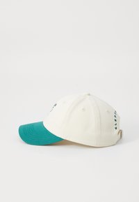 Casquette de baseball en coton avec un couronne crème et une visière bleu sarcelle, ornée d'un texte brodé sur le côté. Sangle ajustable à l'arrière.