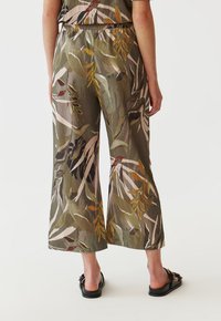 Udbredte bukser i letv�ægtsstof med et grønt og beige bladmønster, elastisk talje og sidelommer. Sorte sandaler fuldender looket.