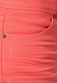 Koraal denim jeans met een gestructureerde afwerking, voorzien van opvallende stiksels, een zijzak en een contrasterende metalen knoop.