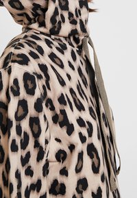 Felpa con stampa leopardata in beige e nero, realizzata in un tessuto testurizzato, con colletto alto e dettagli del laccetto in contrasto.