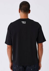 Camiseta de algodón negra de manga corta, con un pequeño estampado de logo blanco en la parte superior de la espalda. Corte regular, textura suave.