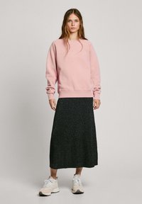 Felpa rosa chiaro con testo in rilievo, abbinata a una gonna midi nera scintillante e sneakers bianche. Outfit casual con texture stratificate.