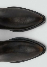 Botas de cuero negro con punta afilada, textura lisa, costuras en contraste y una suela delgada y flexible. La parte superior presenta un acabado elegante.