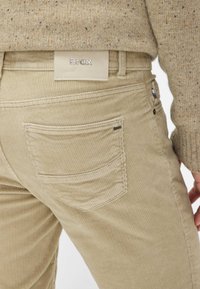 Khaki corduroy broek met een gestructureerde afwerking, voorzien van achterzakken, een leren label met "Brax" en een aansluitend ontwerp.