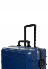 Navy hard-shell suitcase with a textured surface, dual handles, and a retractable black handle labeled "BUILT TO RESIST." Features a combination lock.