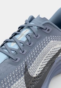 Nike Pegasus running shoe in light blue and gray. Features a breathable mesh upper, textured midsole, and prominent logo accent.