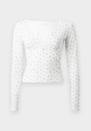 Bílý dlouhý rukáv top s designem do překřížení, zdobený malými modrými květinovými vzory. Vyrobeno z měkké tkaniny s mírně texturovaným povrchem.