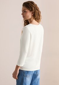 Weißes Langarmshirt mit rundem Halsausschnitt, lockerem Schnitt und glatter Textur, kombiniert mit hellblauen Denim-Hosen mit Gesäßtaschen.