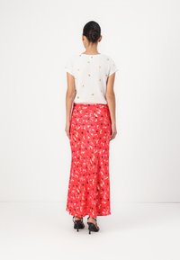 Rode bloemenmaxi-rok met een zachte, vloeiende textuur, gecombineerd met een wit T-shirt met korte mouwen met kleine, kleurrijke patronen.
