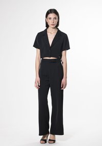 Zwarte cropped shirt met korte mouwen, gecombineerd met hoge taille, wijde zwarte broek. Gladde stof, minimalistisch ontwerp, bijpassende zwarte ceintuur.