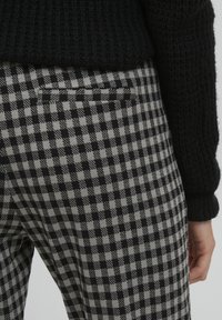 Černé a šedé kostkované kalhoty s zadní kapsou, zkombinované s černým pleteným svetr. Zaměřeno na strukturované pletení a patterned tkaninu.