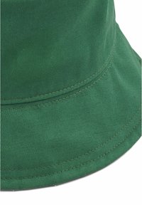 Grön bucket-hatt i texturerat bomullstyg, med en bred skärm och synlig söm längs kanterna för hållbarhet.