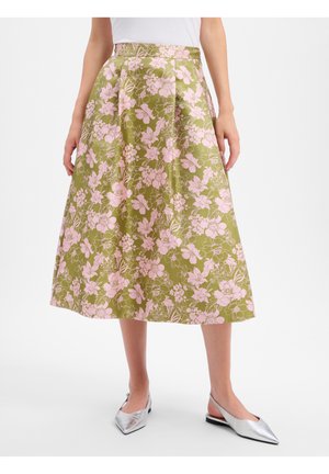 Vrouw draagt een olijfgroene A-lijn rok met lichtroze bloemenprint, gecombineerd met zilvergrijze puntige slingback platte schoenen.