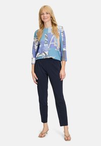 Mehrfarbiger Oberteil mit einem grafischen Druck in Blau, Weiß und Beige, kombiniert mit navyfarbenen Hosen. Leichter Stoff, lockere Passform und Dreiviertelärmel.