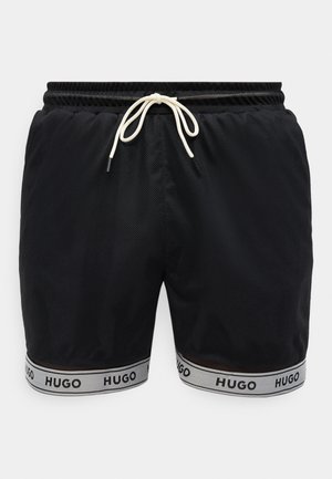 Čierne sieťované šortky s bielym šnúrkovým pásom a bielym lemovaním na nohaviciach so vzorom opakujúceho sa čierneho loga "HUGO".
