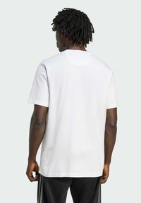 Bílý krátký rukáv, kulatý výstřih, volný střih, vyrobeno z bavlny, hladká textura, jednoduchý design, nošeno s volnými černými kalhotami.