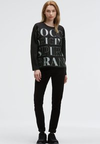 Schwarzer Hoodie mit großem weißem und grauem Grafikspruch, kombiniert mit schwarzen Hosen und schwarzen Sneakers, mit einem lässigen Schnitt und langen Ärmeln.