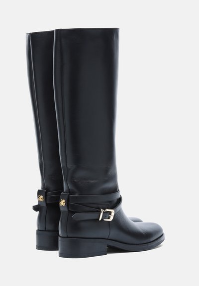 Paire de bottes hautes en cuir noir avec des talons bas blocs, des brides décoratives et des détails de boucles dorées sur fond blanc.