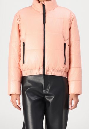 Doudoune courte rose clair avec fermeture éclair noire et poches latérales, associée à un pantalon en cuir noir taille haute sur une personne.