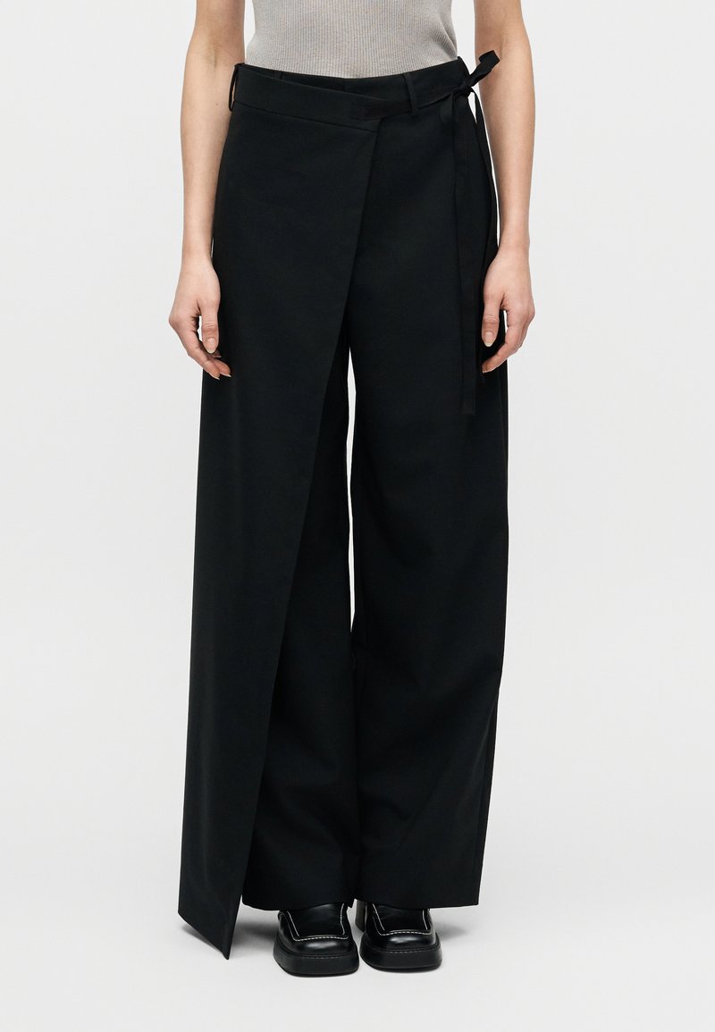 Pantalon noir à jambes larges en tissu structuré, avec ceinture nouée, taille haute et design portefeuille à l'avant.