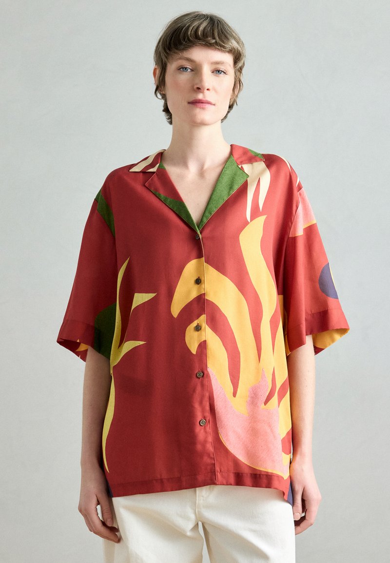 Camicia rossa a maniche corte con audaci motivi astratti gialli e verdi, design con bottoni e colletto. Tessuto liscio con vestibilità comoda.