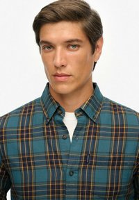 Camisa de cuadros de manga corta con un patrón de cuadros en tonos teal y navy, diseño con cuello y botones en la parte delantera. Fabricada con un tejido suave y texturizado.