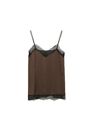 Donna che cammina con una canottiera marrone bordata di pizzo, pantaloni bianchi corti, sandali neri, che porta una grande borsa tote nera intrecciata.
