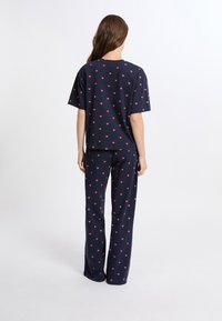 Námořnická pyžamo sada obsahující tričko s krátkým rukávem a dlouhé kalhoty. Oba kousky mají celoplošný vzor růžových srdcí. Měkký bavlněný materiál.