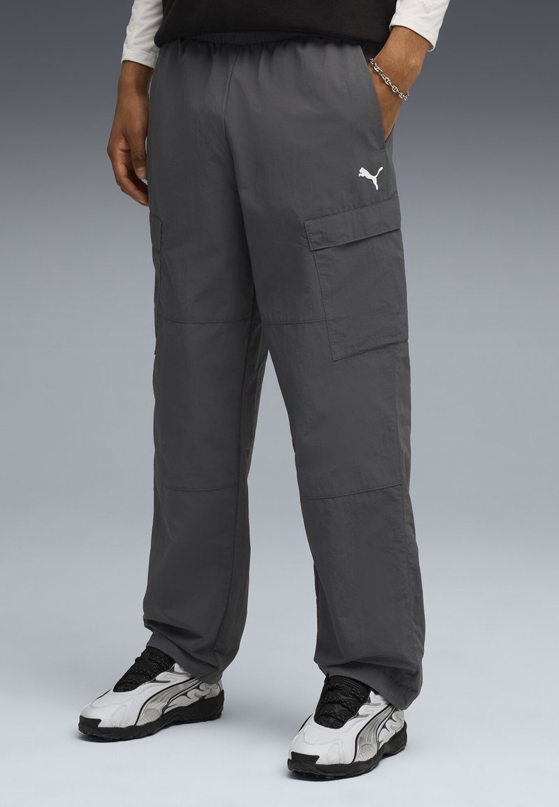 Grå cargo bukser med elastisk talje, med sidelommer og Puma-logo i hvid. Båret med sorte og hvide sneakers.
