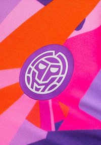 Tissu coloré présentant des motifs géométriques audacieux en rose, orange et violet. Un logo circulaire avec un visage stylisé en blanc et violet.