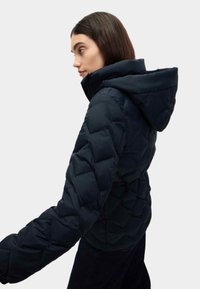 Námořnická modrá péřová bunda s kapucí, vybavená prošívaným designem, elastickými manžetami a střední délkou. Texturovaný materiál má hladký povrch.