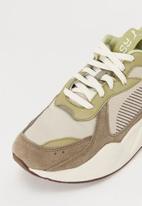 Sneakern har en lättviktsmesh-överdel i beige, olivgröna accenter och brunt mocka. Krämfärgade snören och gummisulan fulländar designen.