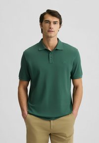 Polo verde realizzato in tessuto morbido, con colletto a tre bottoni, maniche corte e un logo sottile sul petto. Design semplice.