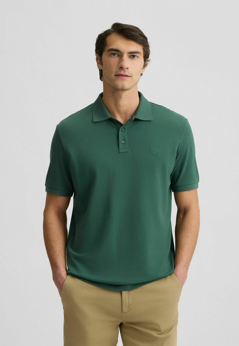 Polo verde realizzato in tessuto morbido, con colletto a tre bottoni, maniche corte e un logo sottile sul petto. Design semplice.
